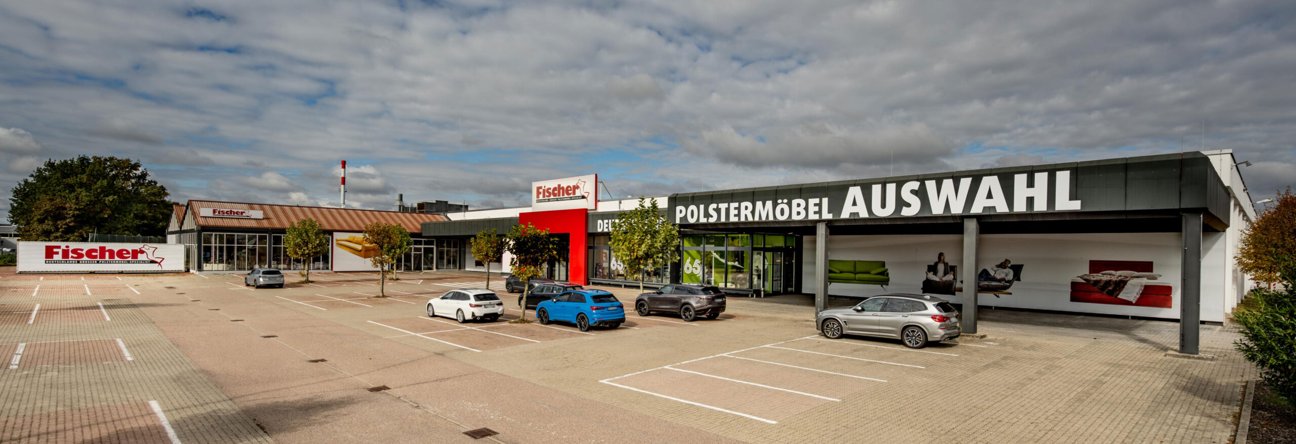 Polstermöbel Fischer Filiale in Bruchsal mit moderner Glasfassade, rotem Eingang und großer Aufschrift ‚Polstermöbel Auswahl‘ – Außenansicht mit Kundenparkplatz.