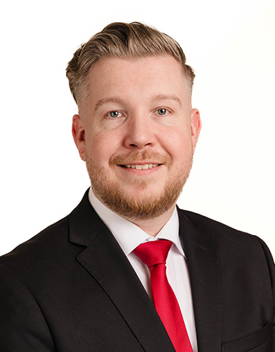 Porträt eines Filialleiters von Polstermöbel Fischer Nürnberg im Business-Anzug mit roter Krawatte vor neutralem Hintergrund.