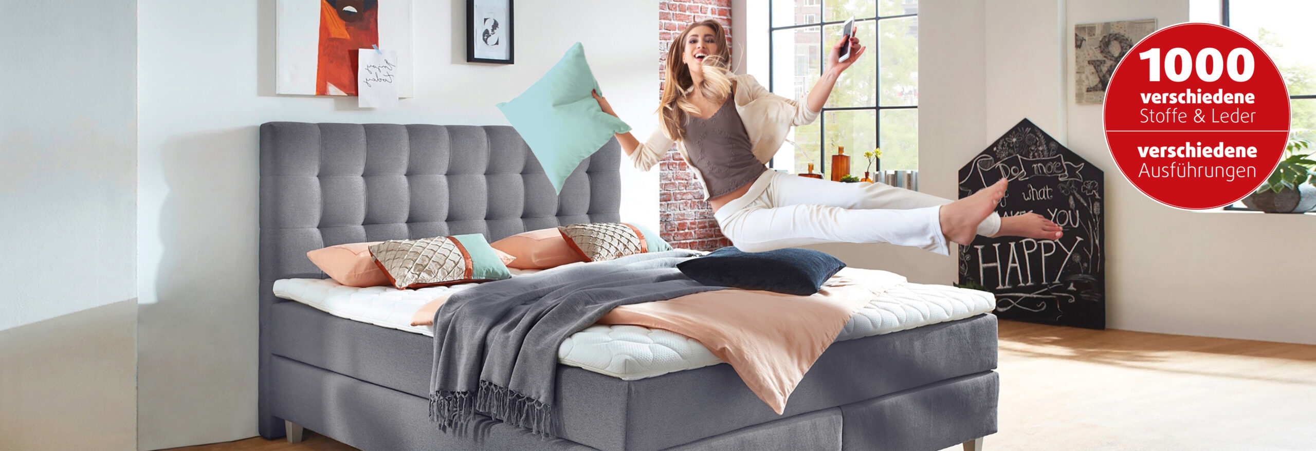 Eine Frau sitzt auf einem grauen Bett in einem modernen Zimmer.