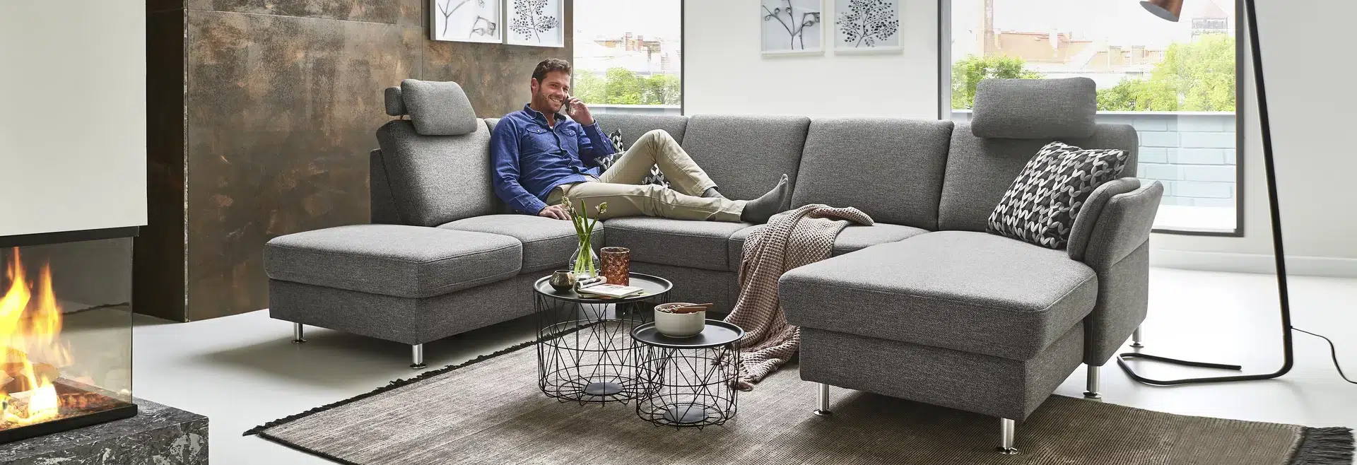 Mann sitzt auf grauem Sofa in gemütlicher Wohnung.