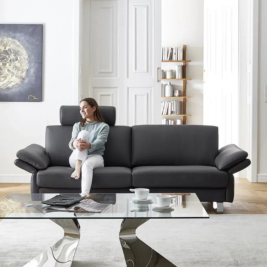 Frau auf schwarzem Sofa in ruhigem Wohnraum.