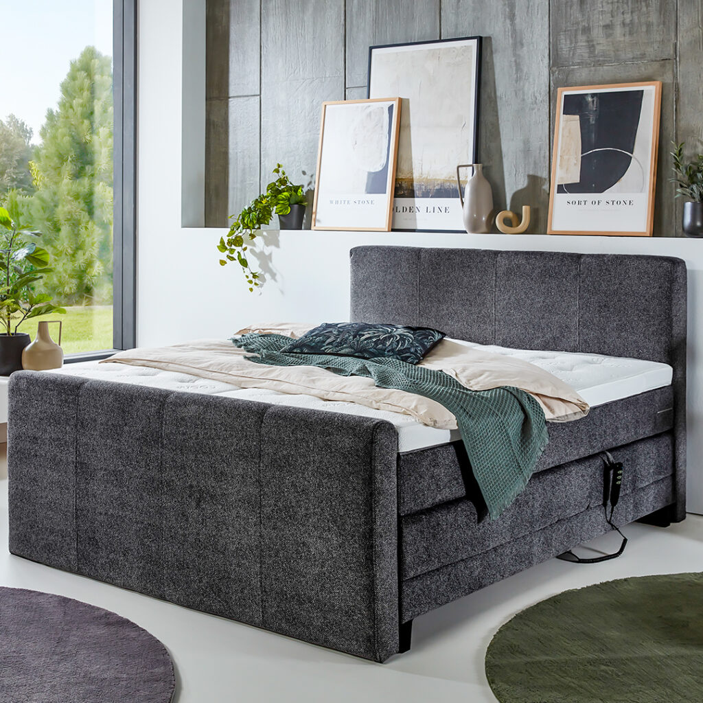 Modernes Boxspringbett in grauem Stoffbezug mit hohem Kopf- und Fußteil, elektrisch verstellbarer Unterbox und stilvoller Schlafzimmerdekoration