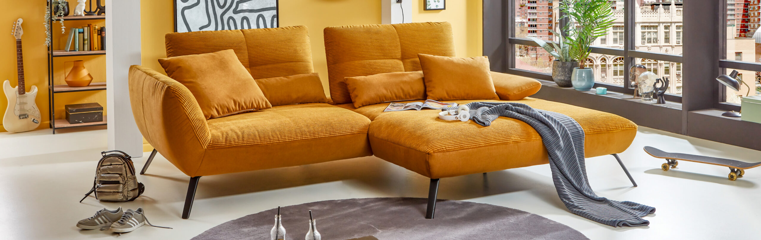 Stylische Wohnlandschaft aus goldgelbem Cordstoff in modernem Wohnzimmer mit urbanem Flair – Sofa mit Relaxfunktion für junge, trendbewusste Einrichter bei Polstermöbel Fischer.