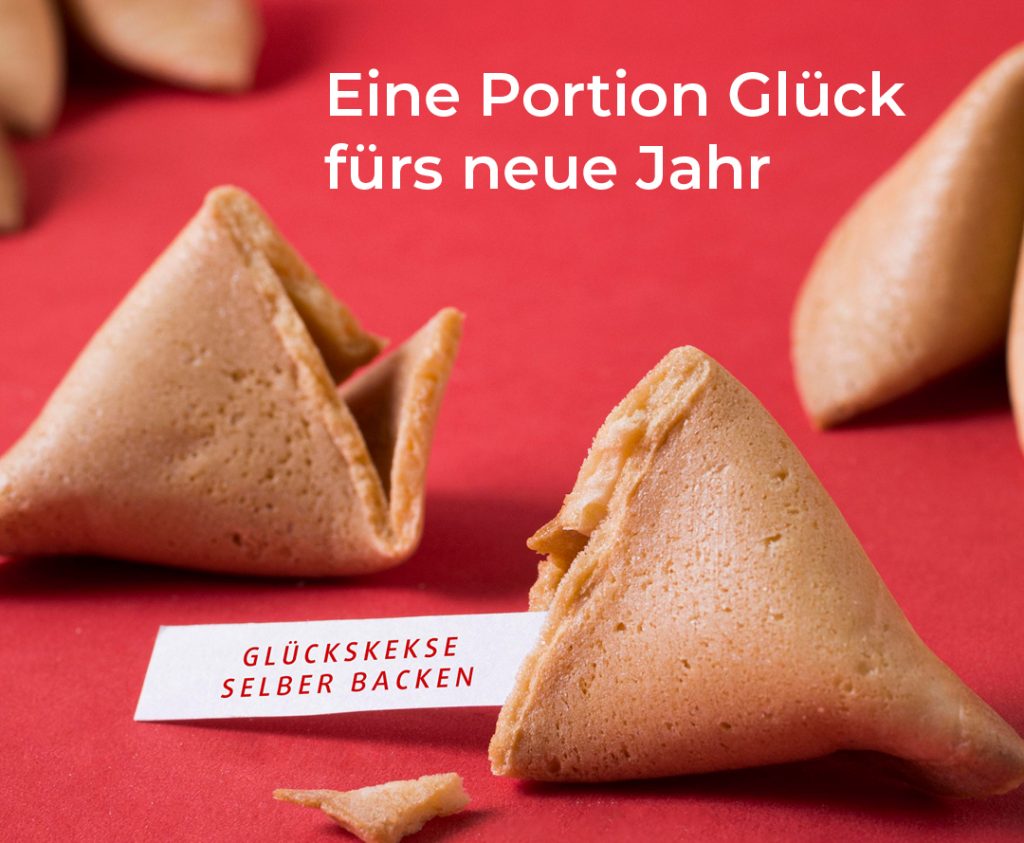 Nahaufnahme von Glückskeksen auf rotem Hintergrund mit Text ‚Eine Portion Glück fürs neue Jahr‘ und Hinweis ‚Glückskekse selber backen‘.