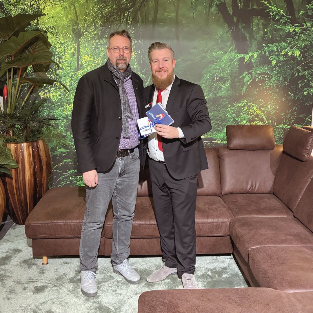 Spendenübergabe von Polstermöbel Fischer an das Martin-Luther-Haus: zwei Männer im Showroom vor brauner Wohnlandschaft mit Kopfstützen