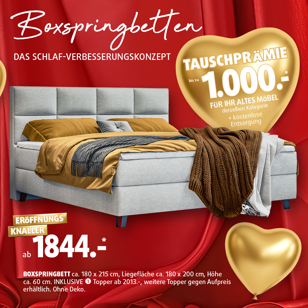 Graues Boxspringbett mit gepolstertem Kopfteil und Decken, präsentiert als Eröffnungsangebot bei Polstermöbel Fischer