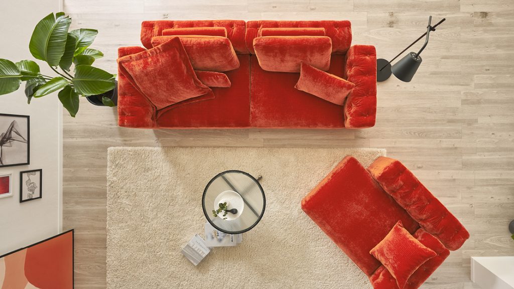 Rotes Designersofa in Draufsicht mit Kissen, Teppich und Wohnaccessoires – ausdrucksstarker Farbtrend für moderne Wohnräume